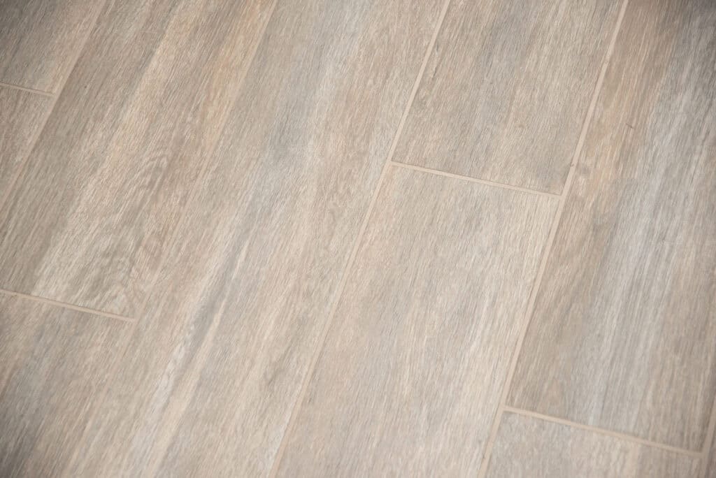 Close-up view of light brown and beige ceramic tiles arranged in a staggered pattern, resembling natural wood flooring with visible grain texture.