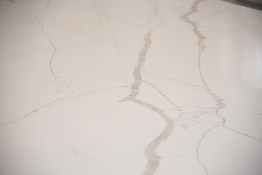 Close-up of a light-colored marble surface with thin, irregular gray veining patterns running across it. The surface appears smooth and polished.