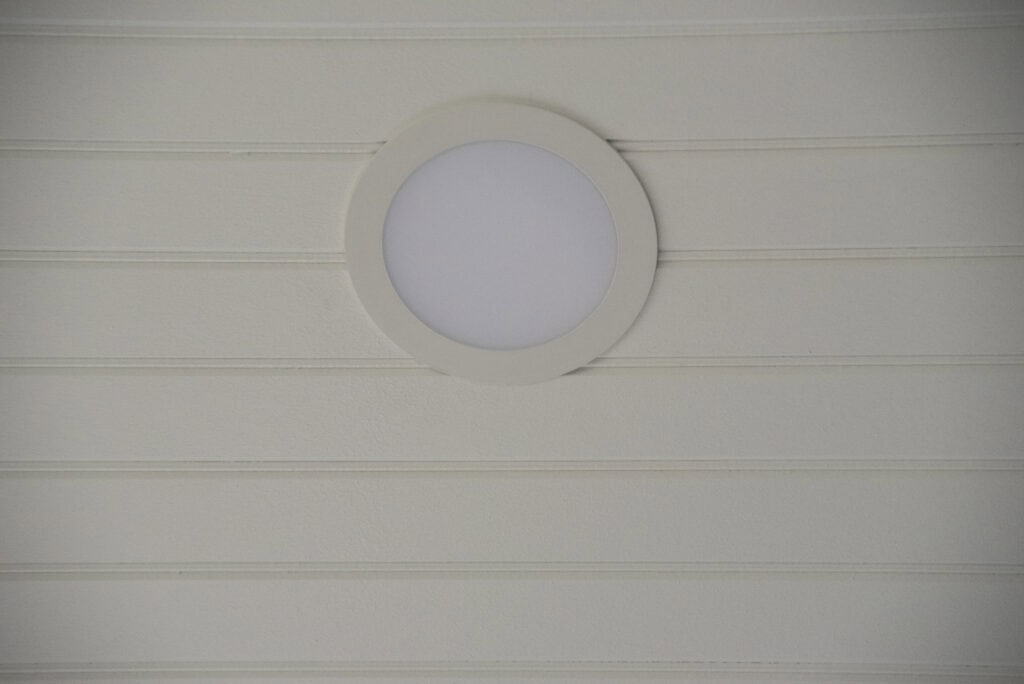 A round white ceiling light fixture is mounted on a light-colored, horizontally paneled ceiling.