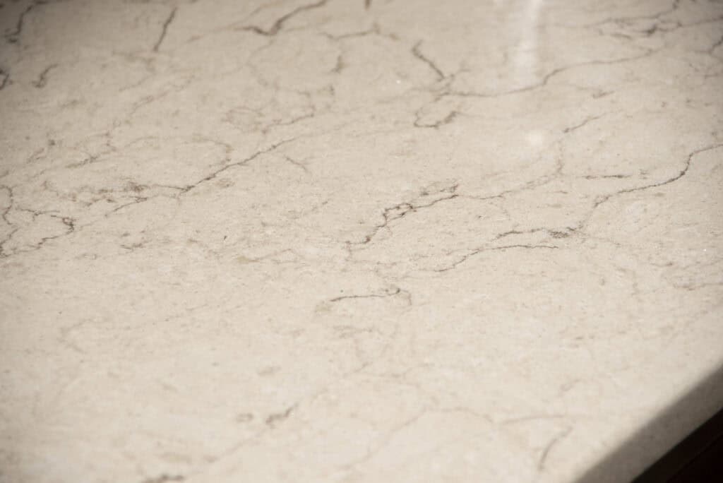 A close-up of a light beige marble surface with subtle gray and brown veining patterns throughout. The smooth finish gives the stone a glossy appearance, highlighting its natural texture and color variations.