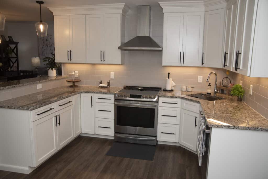 Modern kitchen with white cabinets, stainless steel stove and hood, granite countertops, under-cabinet lighting, and a double sink. The floor is dark wood, and the kitchen is neatly organized.