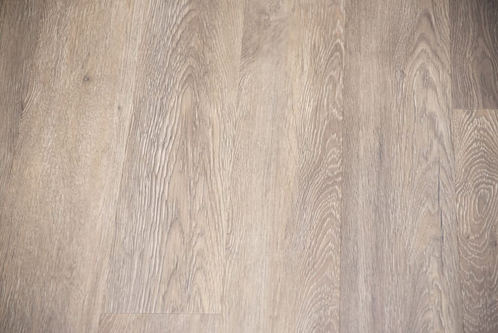 Close-up view of light brown wooden floorboards with visible natural grain patterns and subtle variations in color, giving a warm and textured appearance.