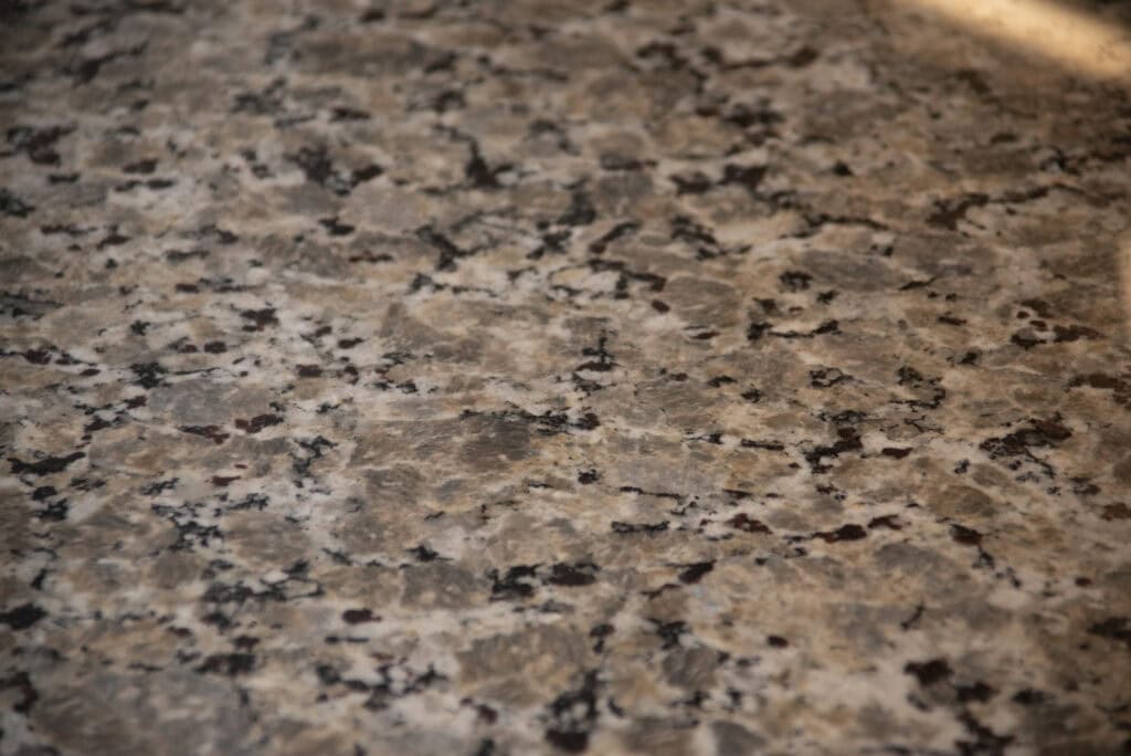 A close-up of a granite countertop with a mottled pattern of beige, brown, black, and gray tones, showcasing a smooth and polished surface.