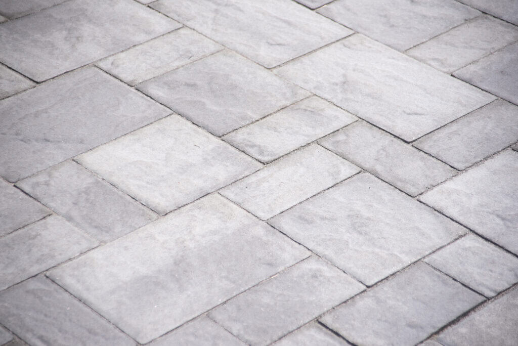 Gray rectangular paving stones arranged in a herringbone pattern, forming a flat, even surface. The stones have subtle texture and varying shades of gray.