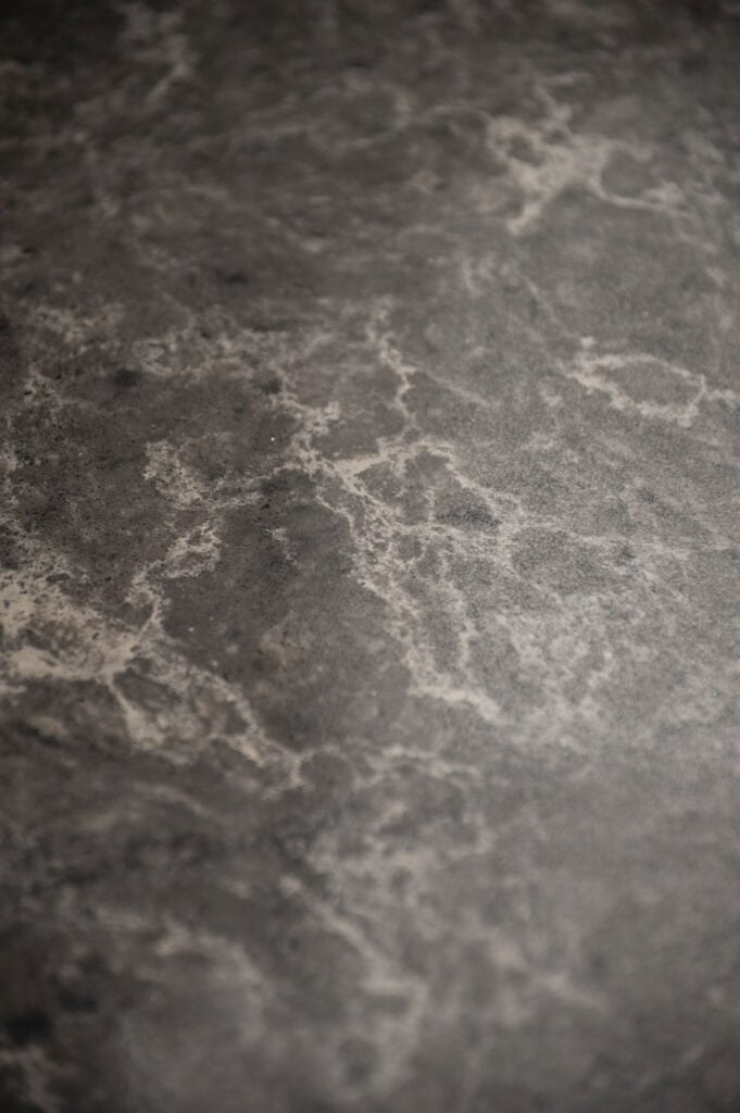 Close-up of a dark gray, marbled stone surface with lighter, irregular veining patterns throughout, creating a natural, textured appearance.