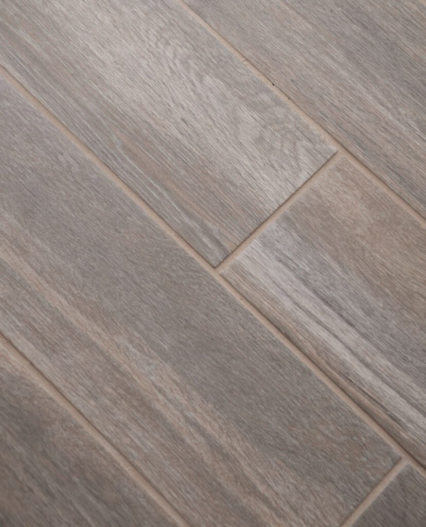 Close-up of a wooden floor with light brown and grayish planks arranged diagonally, showing a natural wood grain texture and subtle color variations.