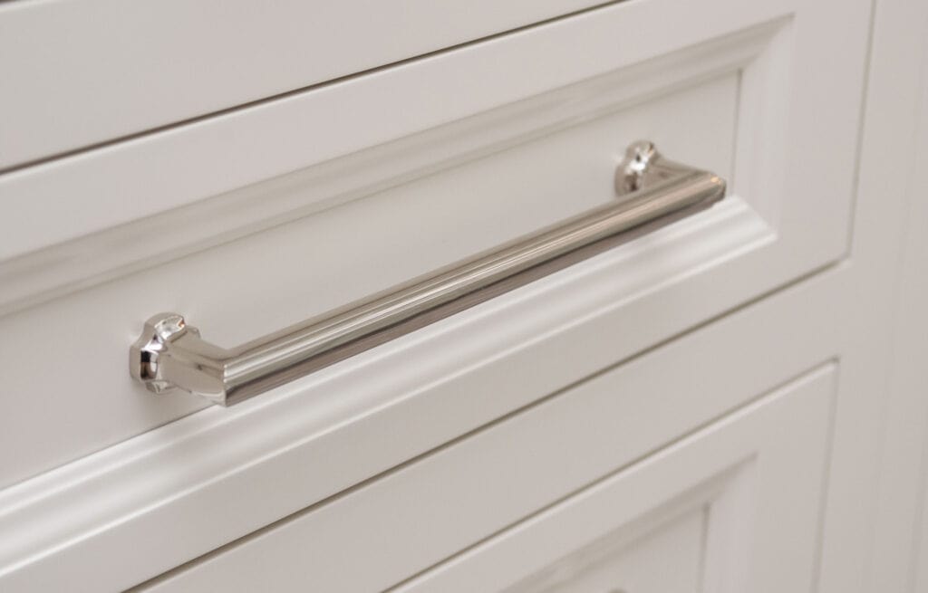 Close-up of a shiny silver drawer handle on a white cabinet with a paneled design.