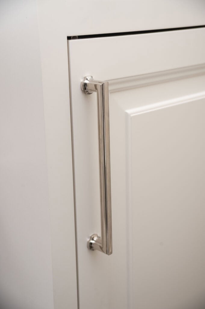Close-up of a white cabinet door with a sleek, modern silver handle attached vertically near the edge.