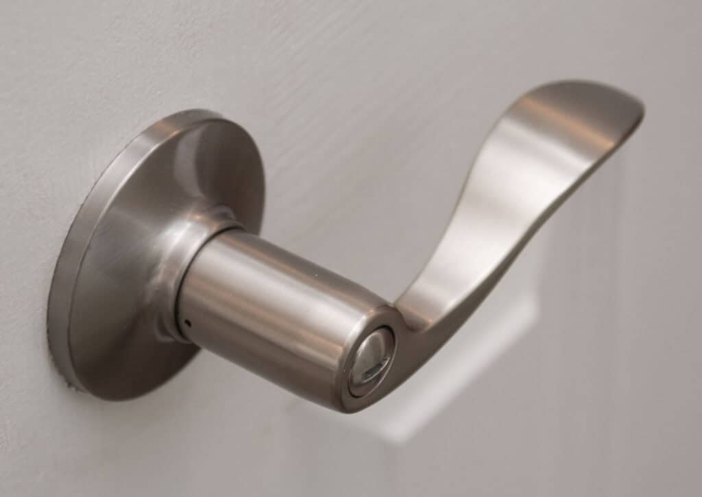 A close-up of a modern, brushed nickel door handle on a white door. The handle has a curved, sleek design and is attached to a round base plate.