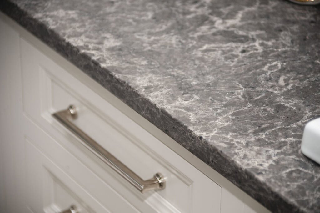 A close-up view of a gray, marble-patterned kitchen countertop above white drawers with a silver handle.
