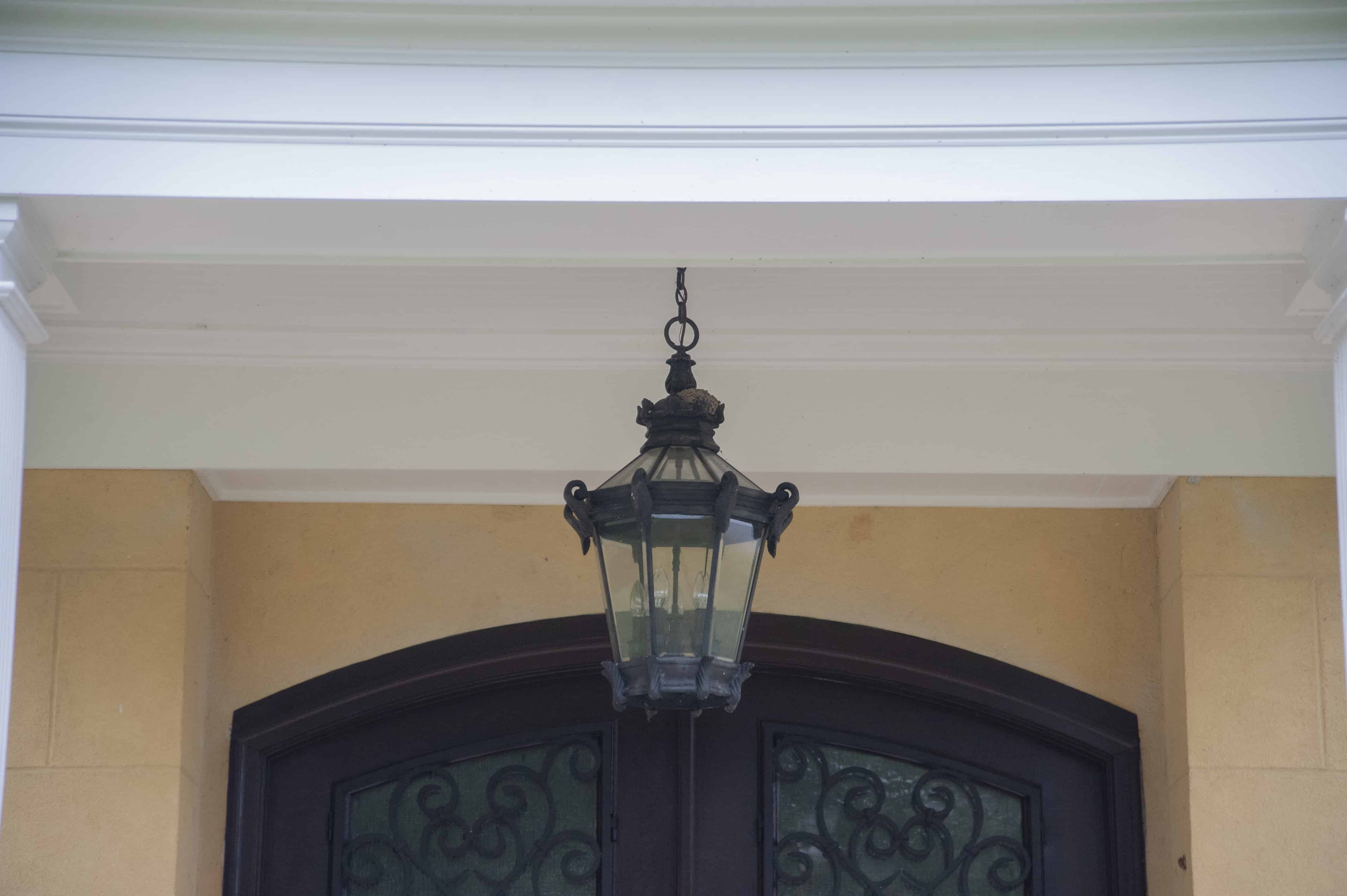 A black metal lantern hangs above a dark arched doorway with decorative glass panels, set against a pale yellow wall and white trim.