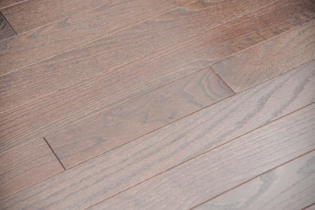 Close-up of a hardwood floor with reddish-brown planks, showing the natural wood grain and texture. The planks are laid side by side with visible seams between them.