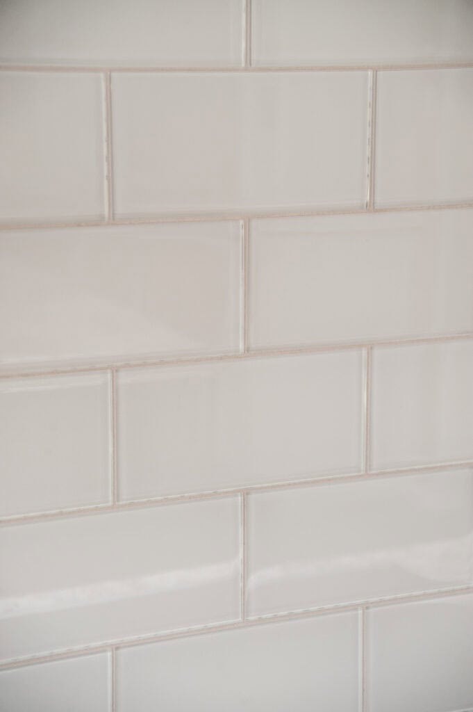 Close-up of a wall with glossy, rectangular white subway tiles arranged in a horizontal, staggered brick pattern. The grout lines are light-colored, giving a clean and modern appearance.