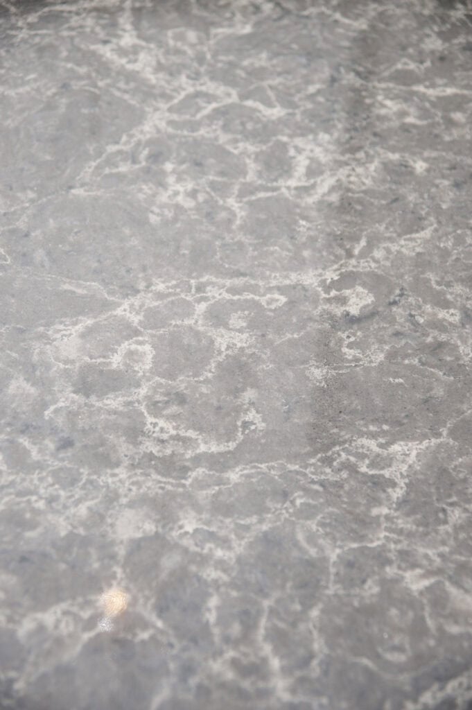 Close-up of a gray marble surface with white veins and a slightly glossy finish, showing natural stone patterns and reflections of light.