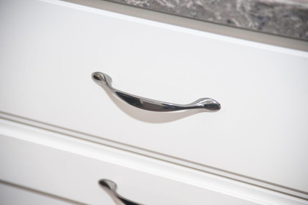 Close-up of a silver metal handle on a white drawer, with a second drawer and part of a marble-patterned countertop visible at the top of the image.