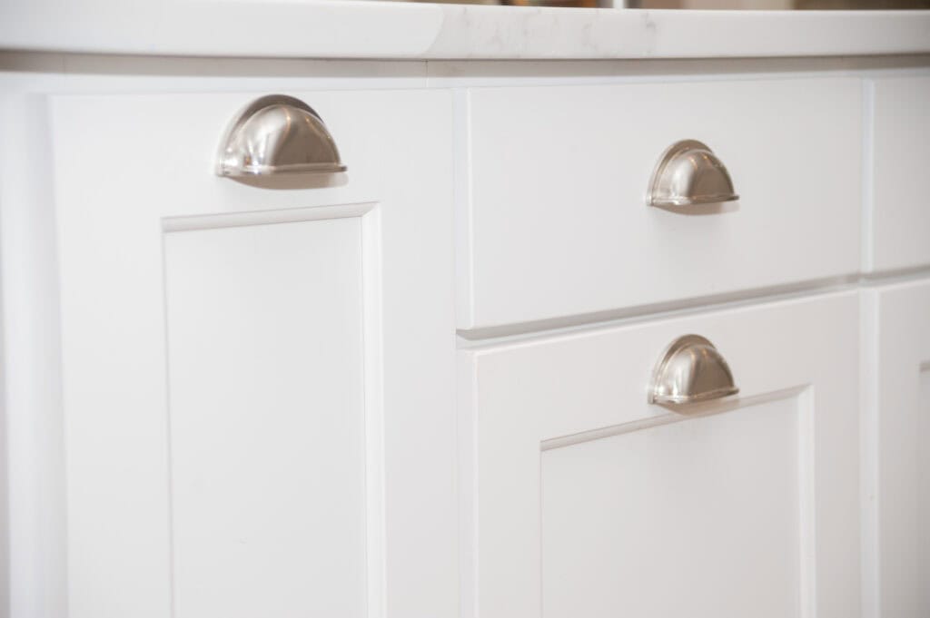 Close-up of white kitchen cabinets and drawers with silver cup-style handles, topped with a white countertop.