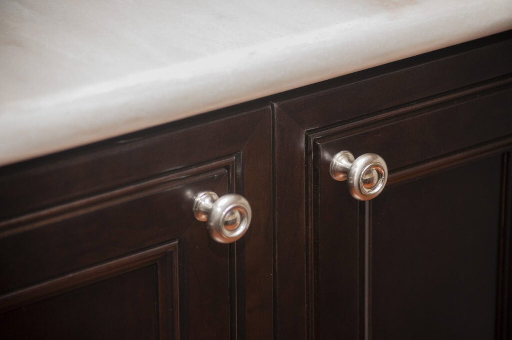 Close-up of two dark wooden cabinet doors with silver round knobs, positioned beneath a light-colored countertop.
