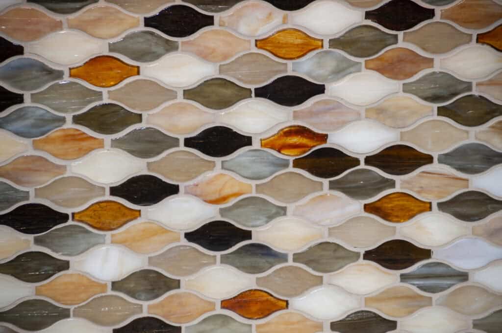A close-up view of a mosaic tile wall with small, leaf-shaped tiles in shades of brown, orange, gray, black, and white, arranged in a repeating, interlocking pattern.