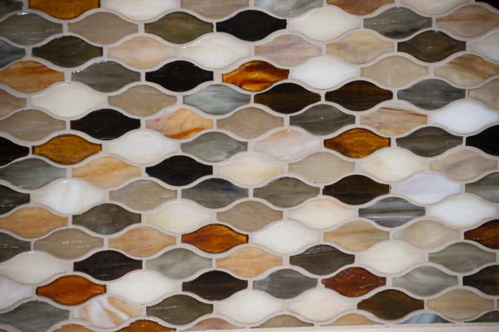 A close-up of a tile mosaic featuring leaf-shaped tiles in various earthy tones, including brown, tan, white, cream, gray, and amber, arranged in a repeating, interlocking pattern.