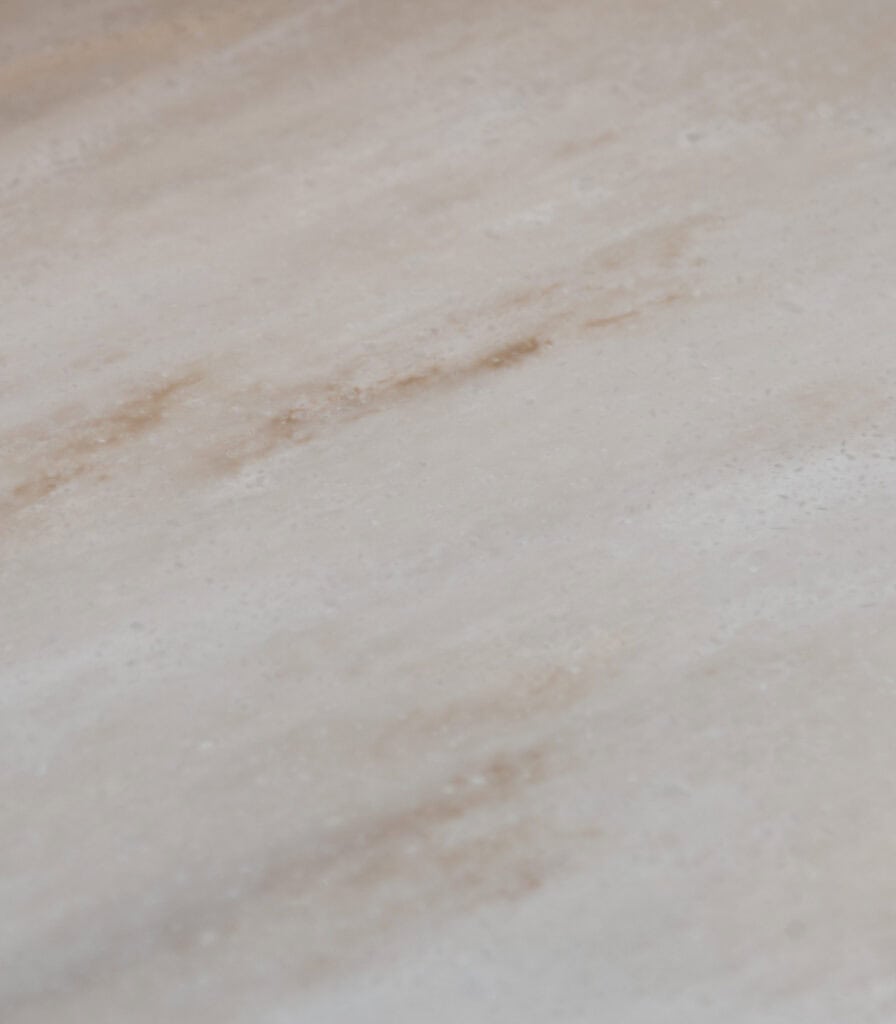 A close-up of a light-colored marble surface with subtle beige and brown streaks and natural, smooth texture.