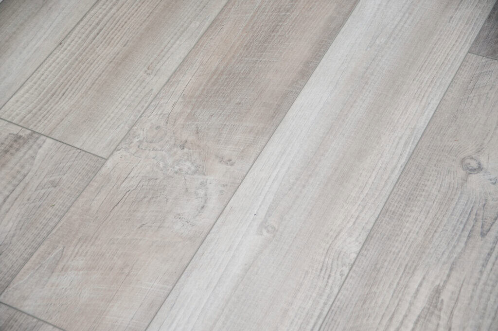 A close-up view of light-colored wooden floor planks with visible grain patterns and knots, arranged in a staggered pattern.