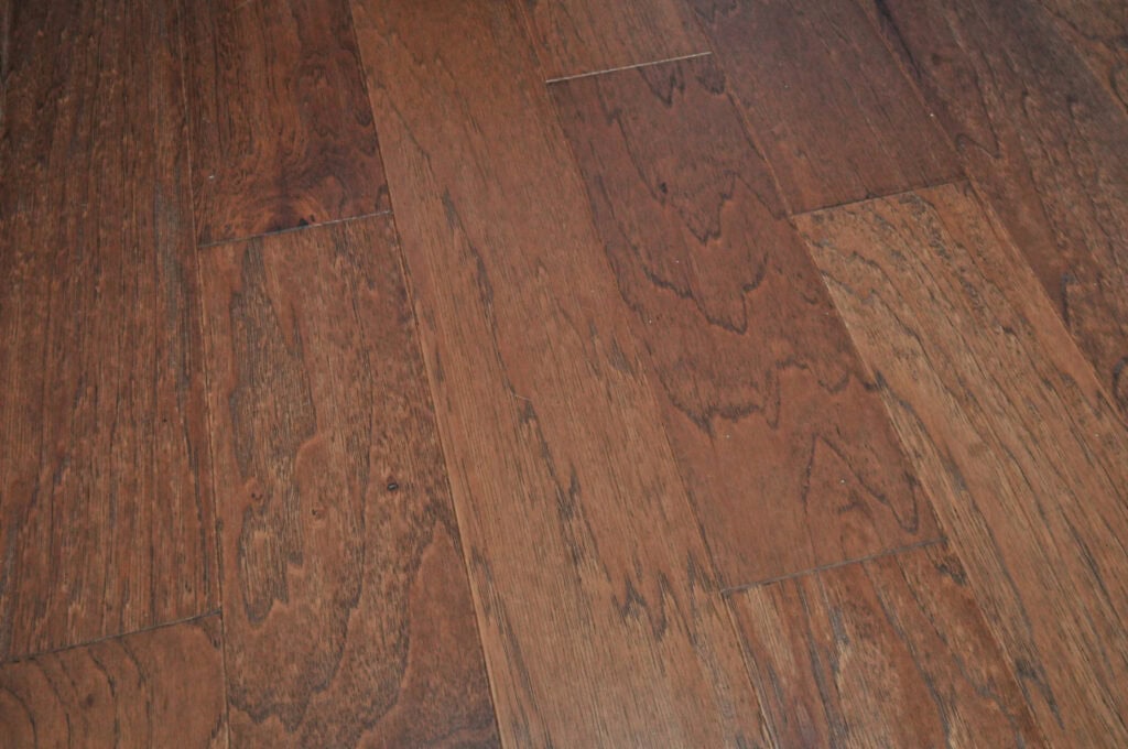Close-up view of medium-brown wooden floor planks with visible natural grain patterns and slight color variations. The planks are arranged in a staggered layout.
