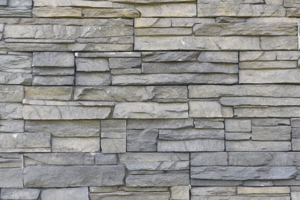 A close-up view of a wall made of gray rectangular stone bricks arranged in a staggered pattern, showing rough textures and varying sizes.
