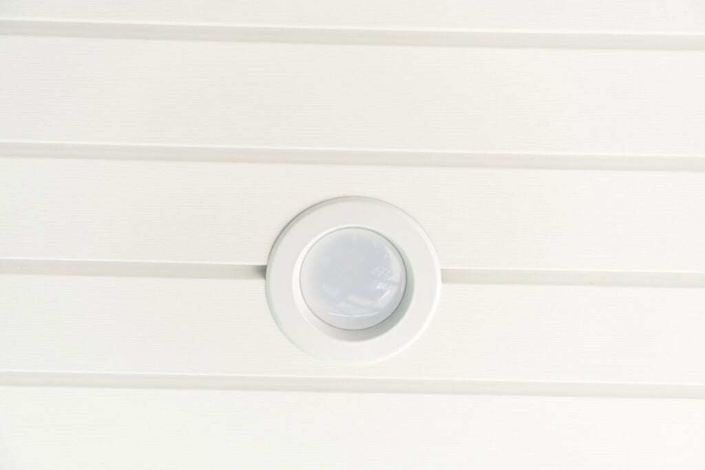 Close-up of a round, white recessed ceiling light fixture mounted on a white paneled ceiling.