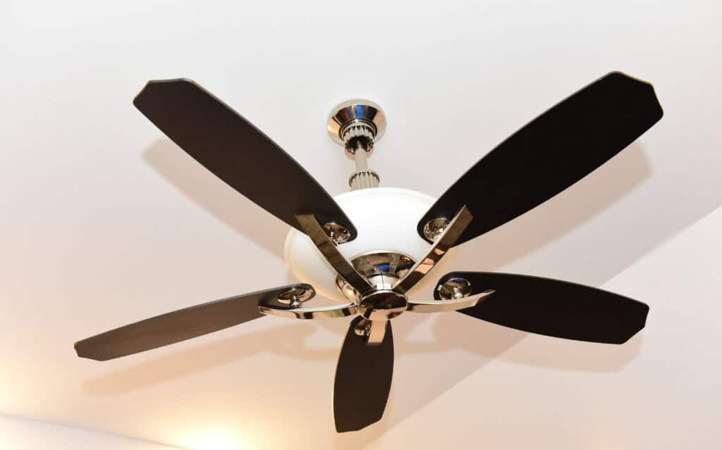 A modern ceiling fan with five dark blades and a white light fixture is mounted on a white ceiling.