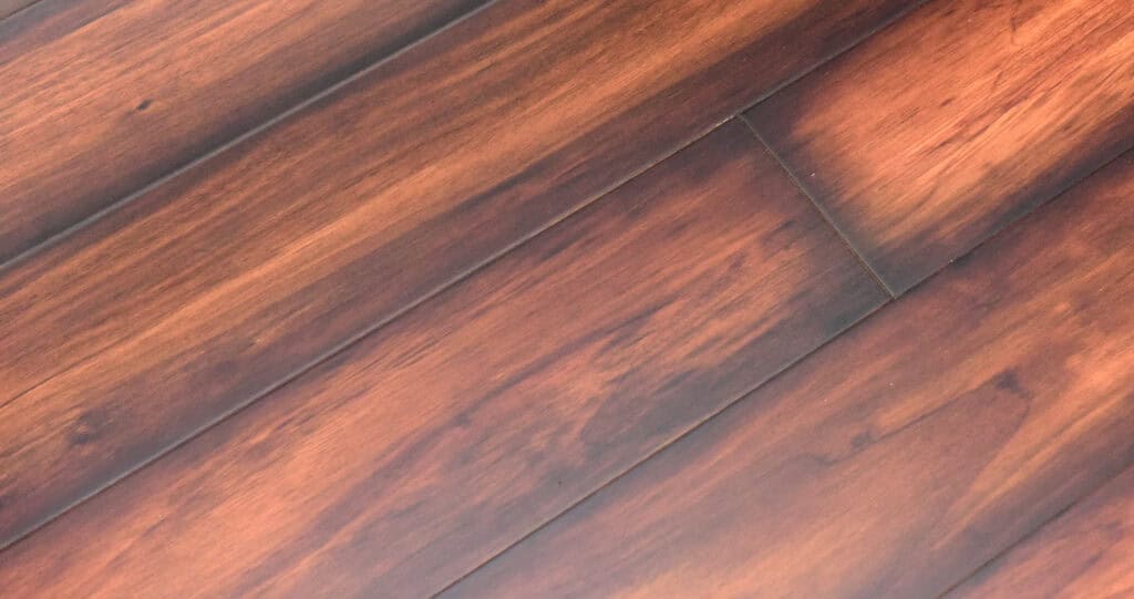 Close-up view of reddish-brown wooden floorboards with natural grain patterns and a smooth, glossy finish. The boards are arranged diagonally across the image.