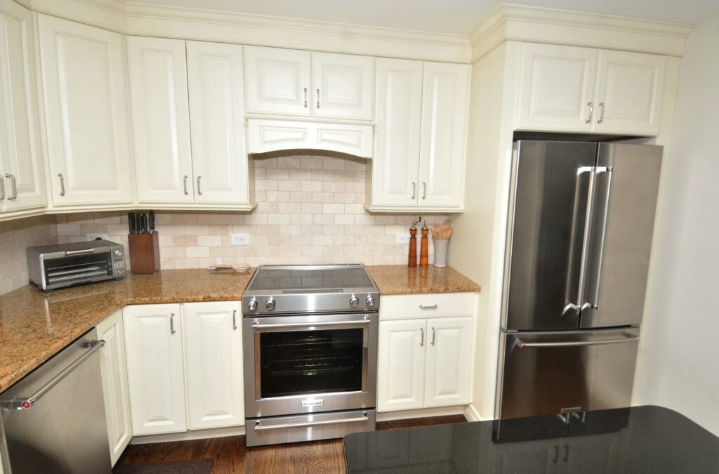 A modern kitchen with white cabinets, stainless steel appliances including a stove and refrigerator, granite countertops, a toaster oven, knife block, and spice containers on the counter.