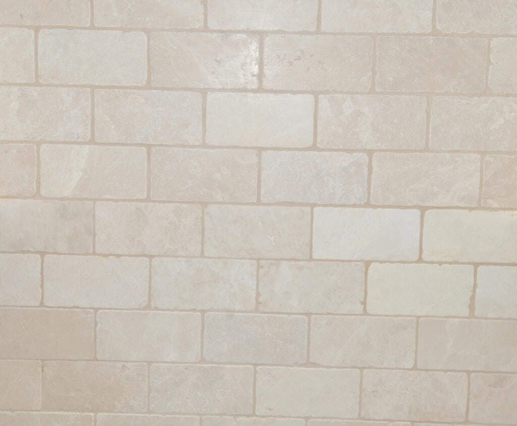 A close-up view of a beige tiled wall with rectangular tiles arranged in a staggered brick pattern. The tiles have subtle variations in color and texture.