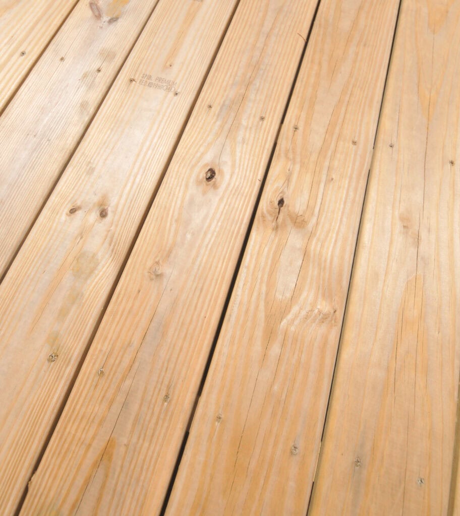 Close-up view of light-colored wooden planks arranged side by side, showing natural wood grain patterns and knots, with visible nails securing the boards.