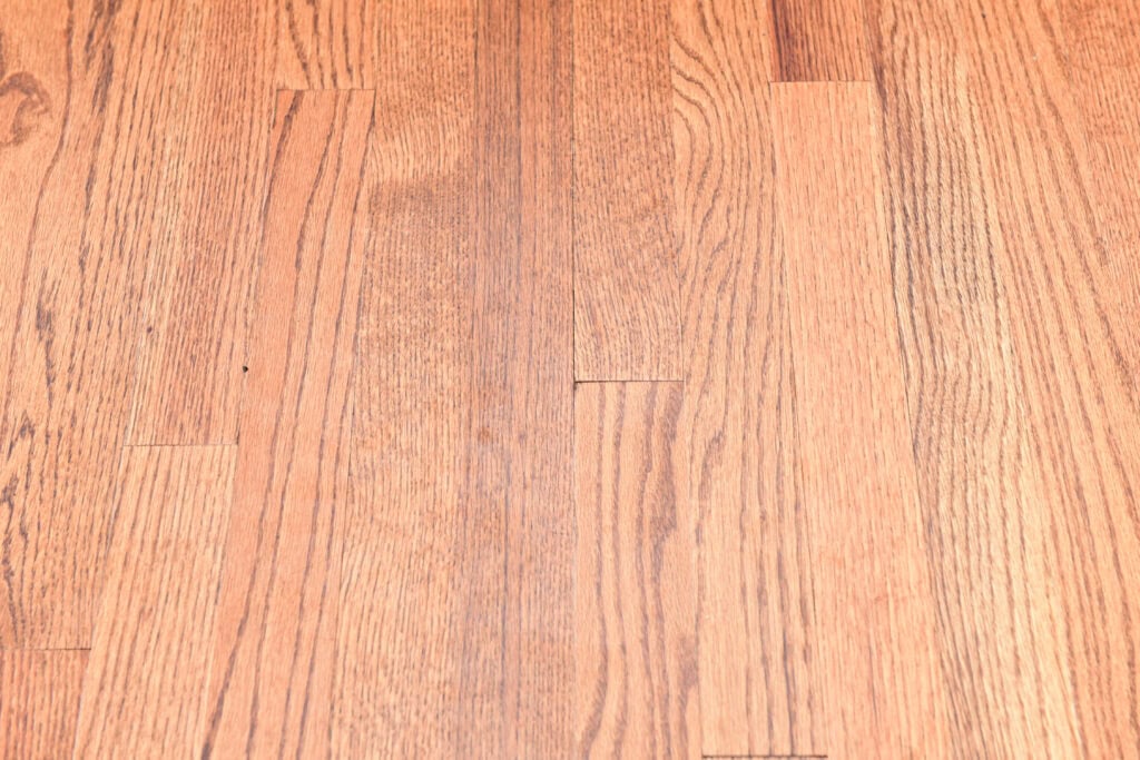 Close-up view of light-colored hardwood flooring with visible grain patterns and slight gaps between some of the planks.