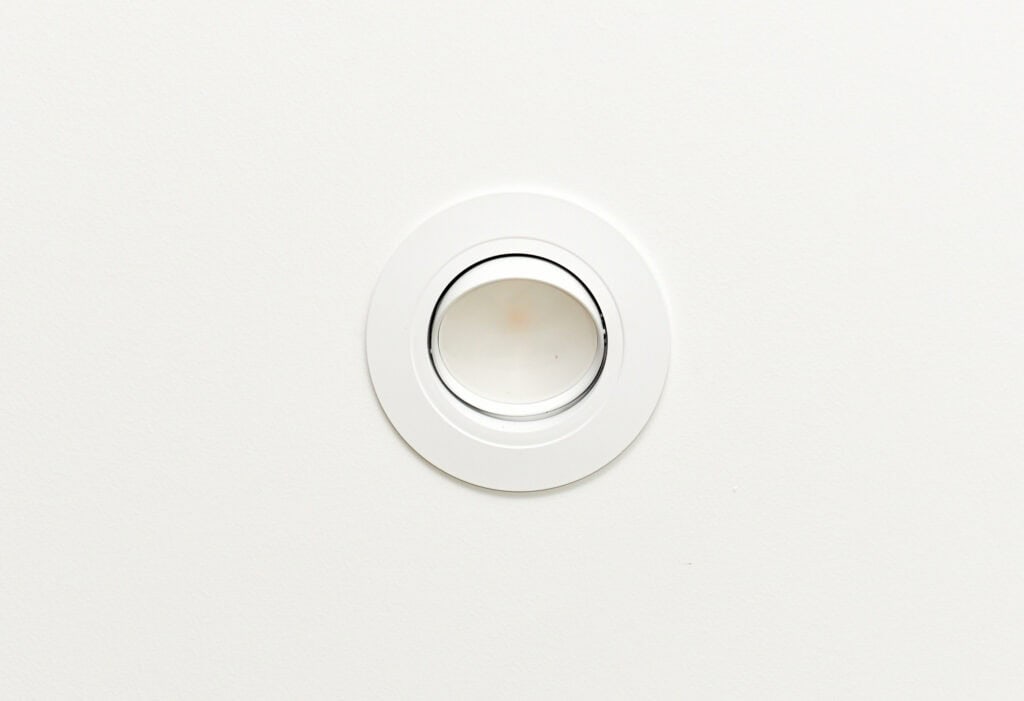 A round, recessed ceiling light with a white trim set into a plain white ceiling.