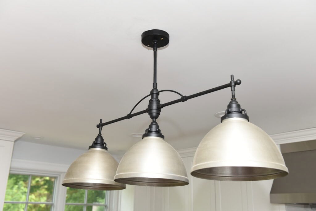 A black metal ceiling light fixture with three large, dome-shaped, brushed metal lampshades hanging over a white ceiling in a modern room.