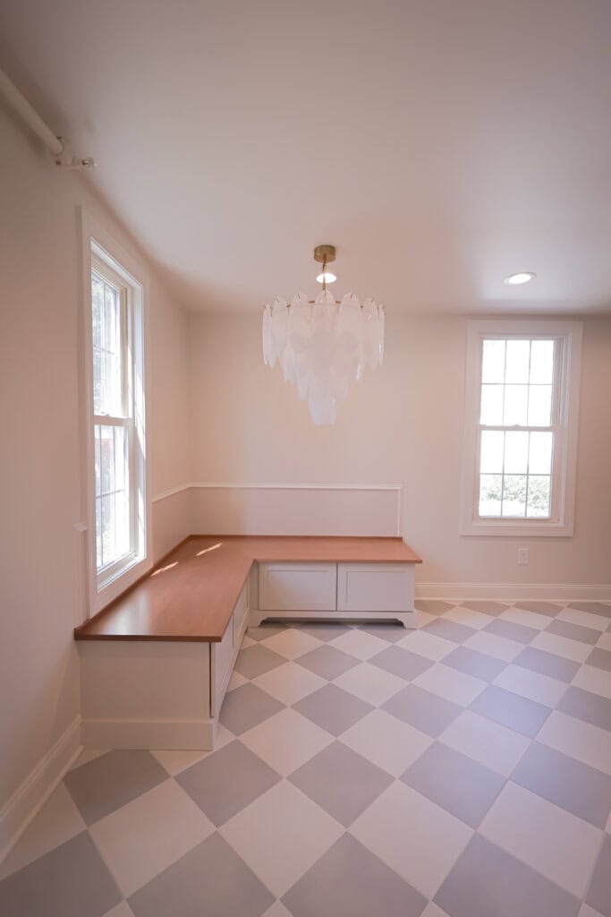 a bright room with two large windows, a corner wooden bench with storage drawers, a modern chandelier, and a floor with a gray and white diamond pattern.