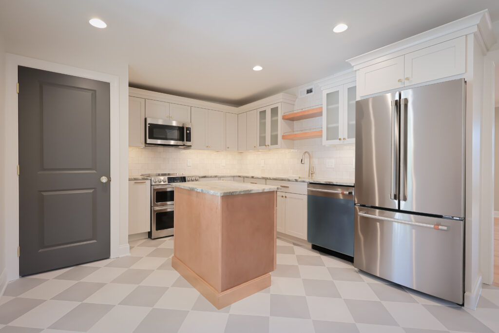 modern kitchen with white cabinets, marble island, stainless steel appliances, gray door, light tile floor, and under cabinet lighting. the space feels clean, bright, and contemporary with a central small island.