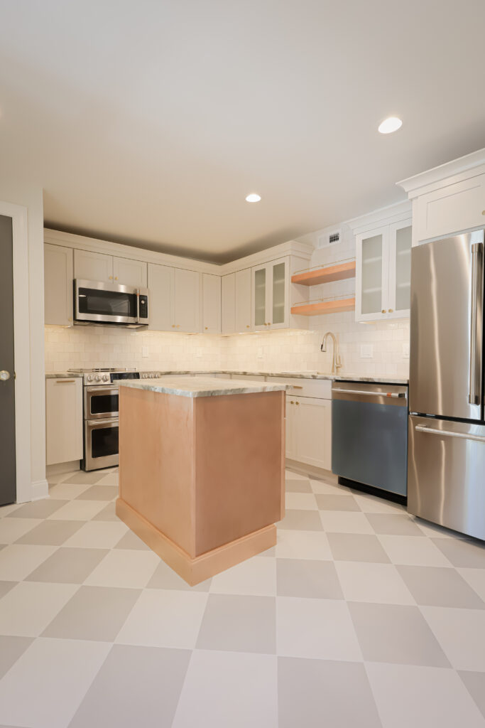 modern kitchen with white cabinets, stainless steel appliances, a marble topped island with a copper base, checkered floor tiles, and open wood shelves. the kitchen is brightly lit with recessed ceiling lights.