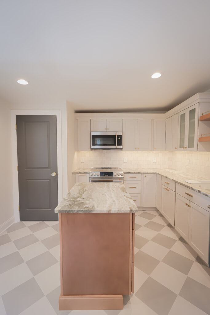 modern kitchen with white cabinets, gray door, checkered tile floor, marble island, built in microwave, stove, and under cabinet lighting. shelves and countertop space are visible. room is brightly lit with recessed lights.