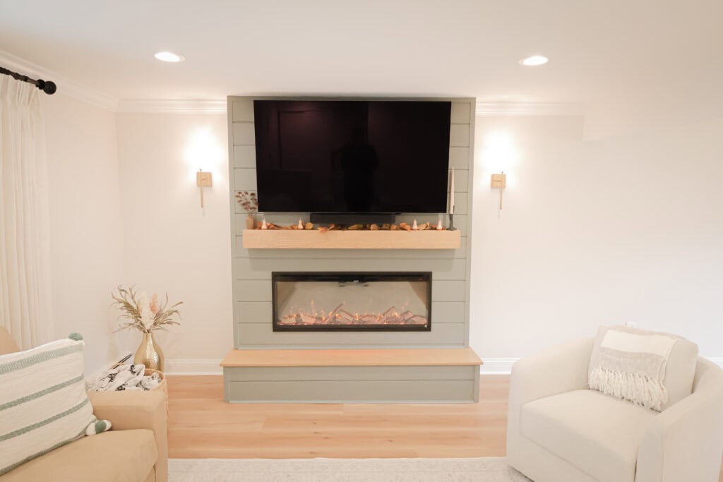 A modern living room features a wall-mounted TV above a built-in electric fireplace with decorative stones, surrounded by neutral furniture and soft lighting.