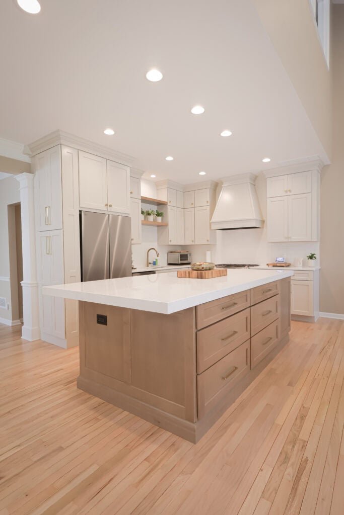 modern kitchen with light wood floors, white cabinets, stainless steel appliances, and a large island with a white countertop and built in drawers. recessed ceiling lights brighten the space.