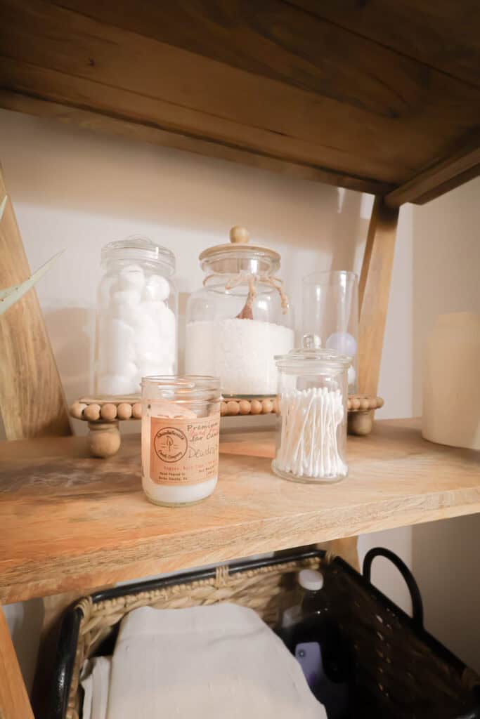 Decorative candles and jars on wooden shelf in bathroom.