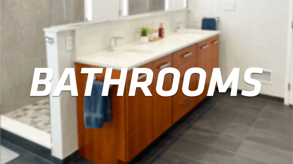 Modern bathroom with double sinks, wooden cabinets, dark tiled floor, and a glass-enclosed shower. The word “BATHROOMS” is overlaid in bold white text across the image.