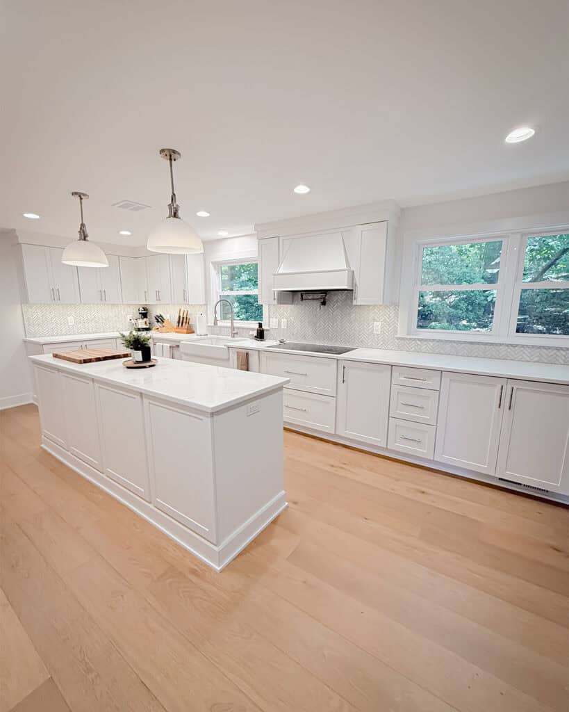 Bright, modern kitchen with white cabinets, a large island, stainless steel appliances, pendant lights, light wood floors, and large windows letting in natural light.