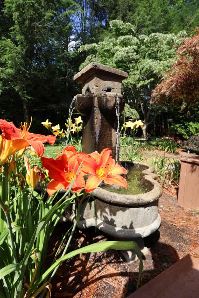 Decorative garden fountain surrounded by colorful flowers and lush greenery.