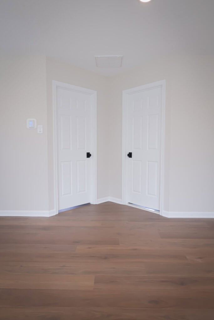 Interior view of bathroom with two white doors and hardwood flooring.