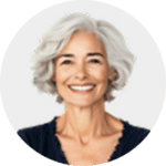 Smiling older woman with short, wavy gray hair, wearing a dark top, pictured against a light, plain background.