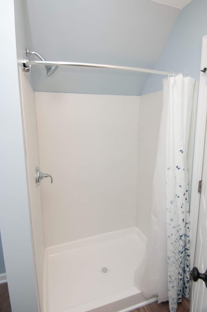 A clean, white shower stall with a curved shower rod, a partially closed white shower curtain with blue patterns, silver shower fixtures, and light blue walls.