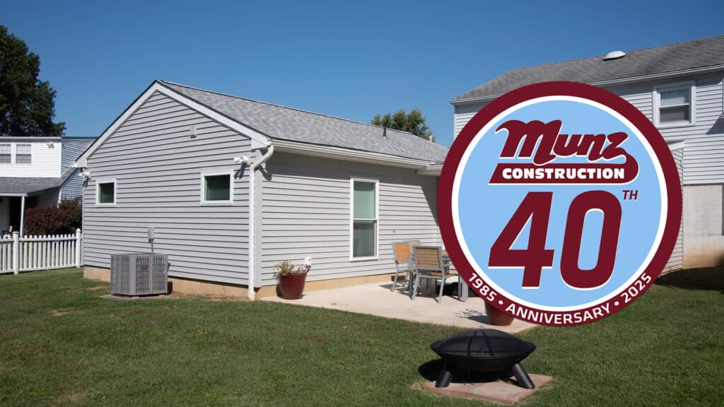 A gray single-story house with a patio, outdoor furniture, and a fire pit in the backyard. Considering how to add an in-law suite? An emblem in the foreground reads Munz Construction 40th Anniversary 1985-2025.
